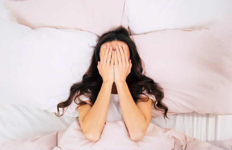 Крупным планом фото молодой женщины с вьющимися каштановыми волосами, которая лежит в постели